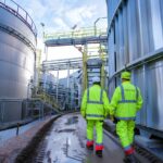 two men walking between metal silos